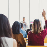 Back view woman raising hand for asking speaker for question and answer concept in meeting room for seminar